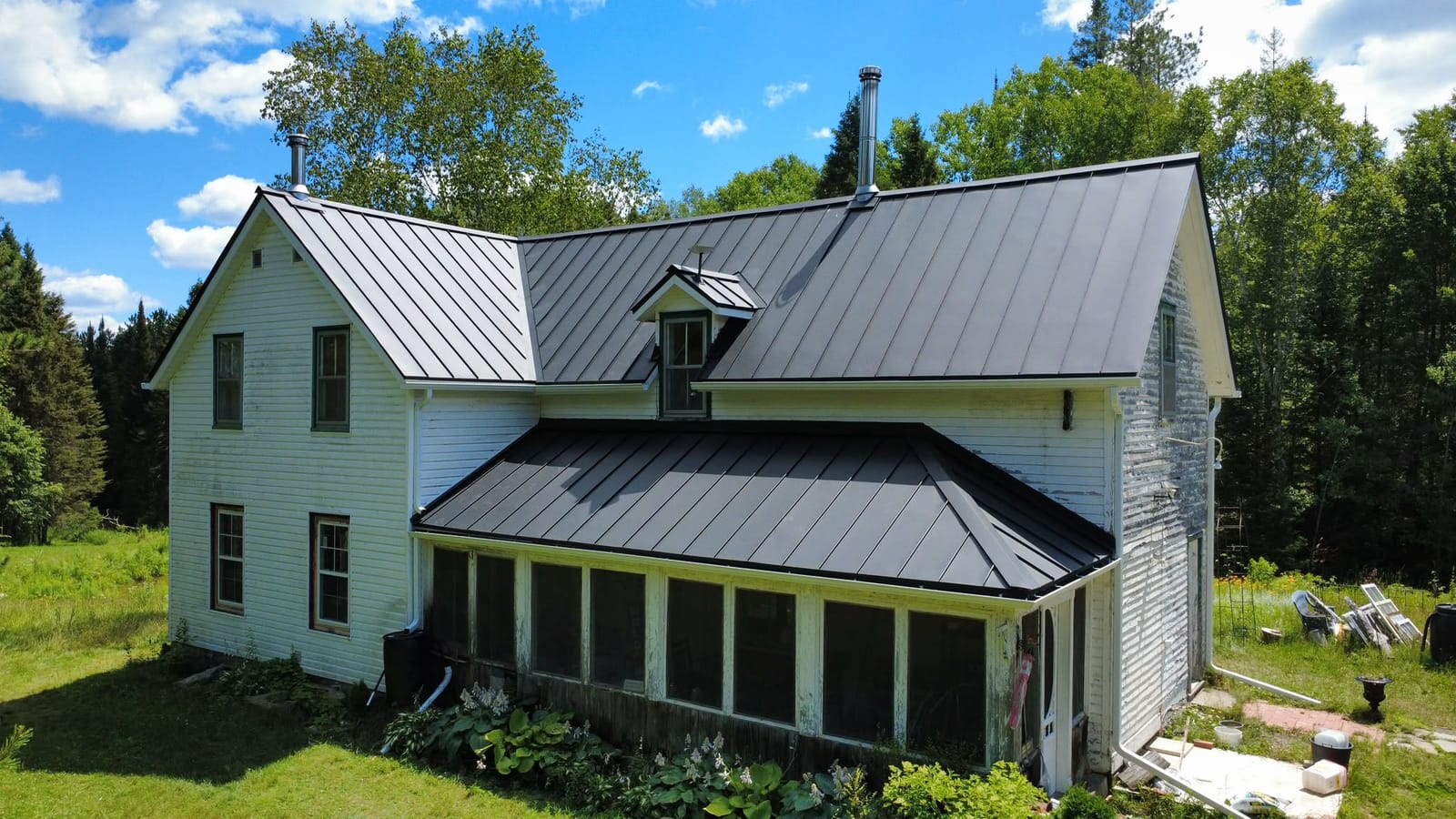Aerial view of a white century farmhouse in Ontario with a new charcoal standing seam metal roof covering the main house, dormer and enclosed sunroom