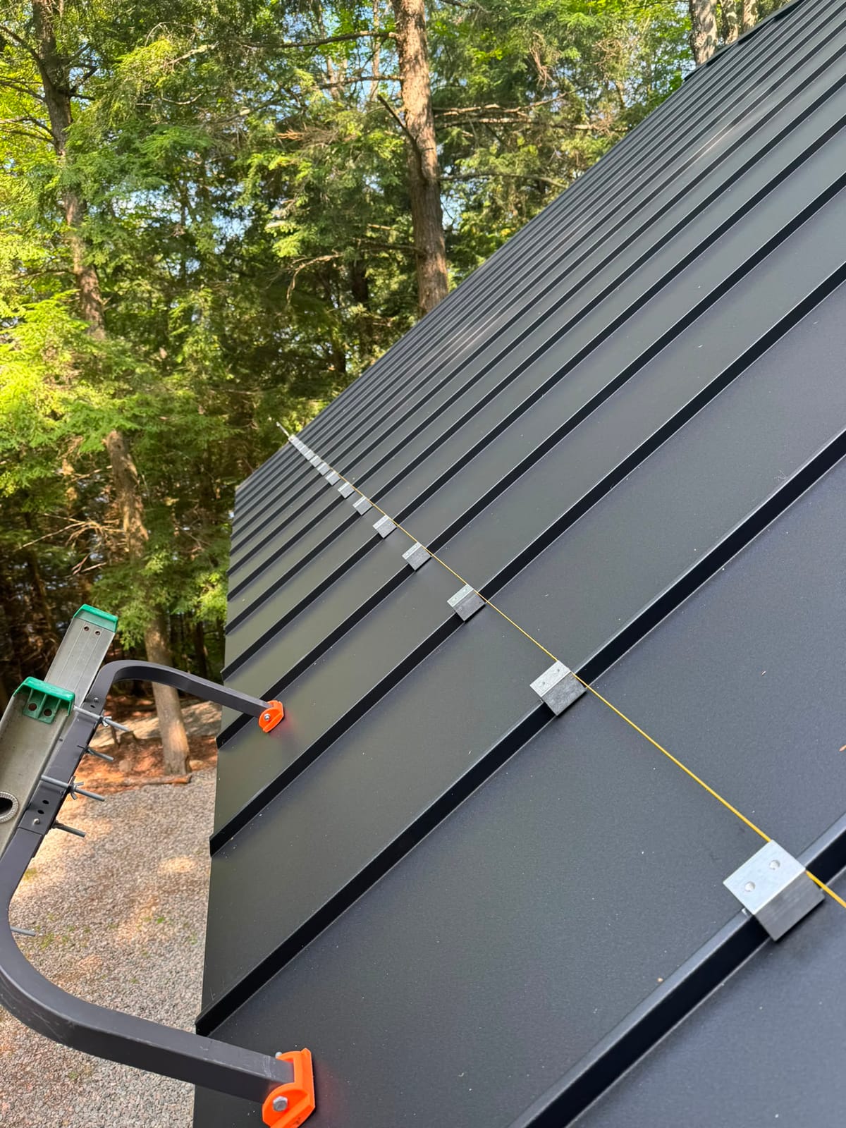 Concealed metal clips and a string line laid out across charcoal standing seam panels during installation, showing clip spacing